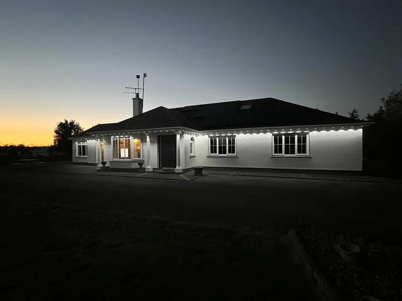 White Govee roofline lights illuminating the front and side of the showcase bungalow at sunset